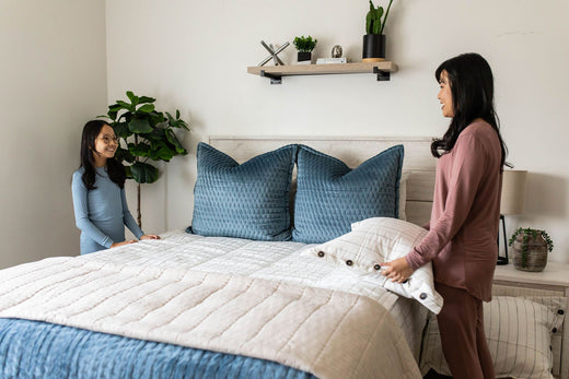 
      a mother and daughter making the bed together using neutral zipper bedding and blue throw pillows and blankets.
    