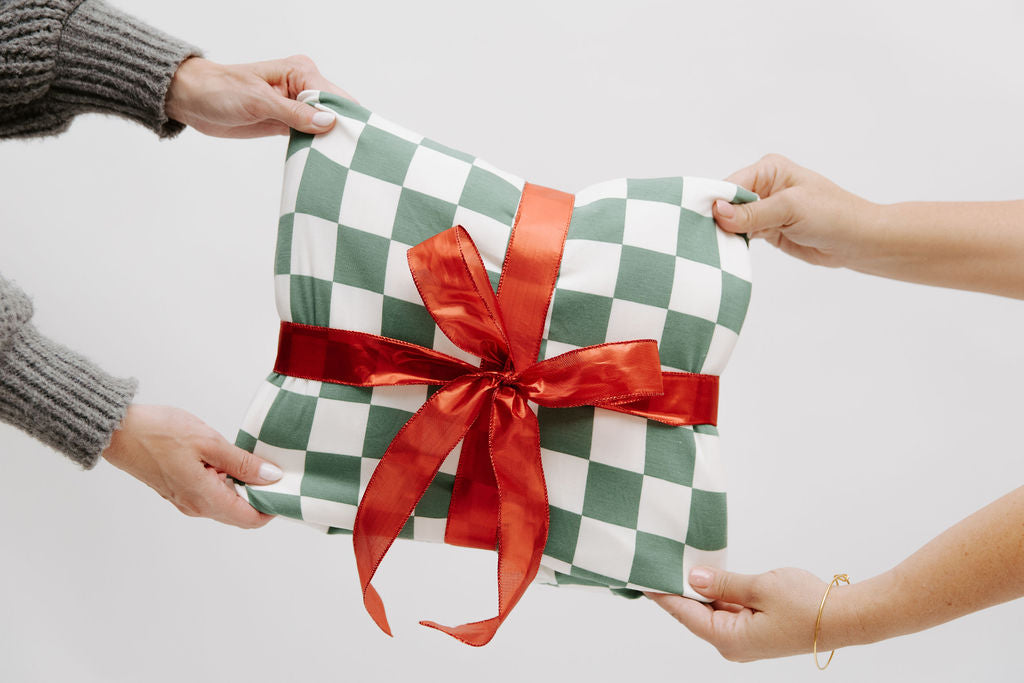 
      a green and white checked blanket wrapepd in a red bow being passed to someone
    