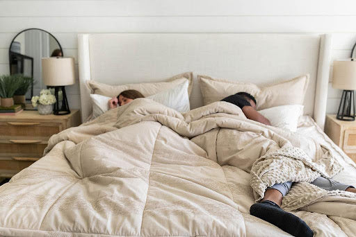 
      A man and woman asleep in. a bed with gray Beddys bedding and a neutral bed frame.
    