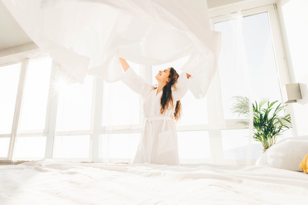 
      A woman spreading fresh sheets onto her bed in a brightly lit bedroom.
    