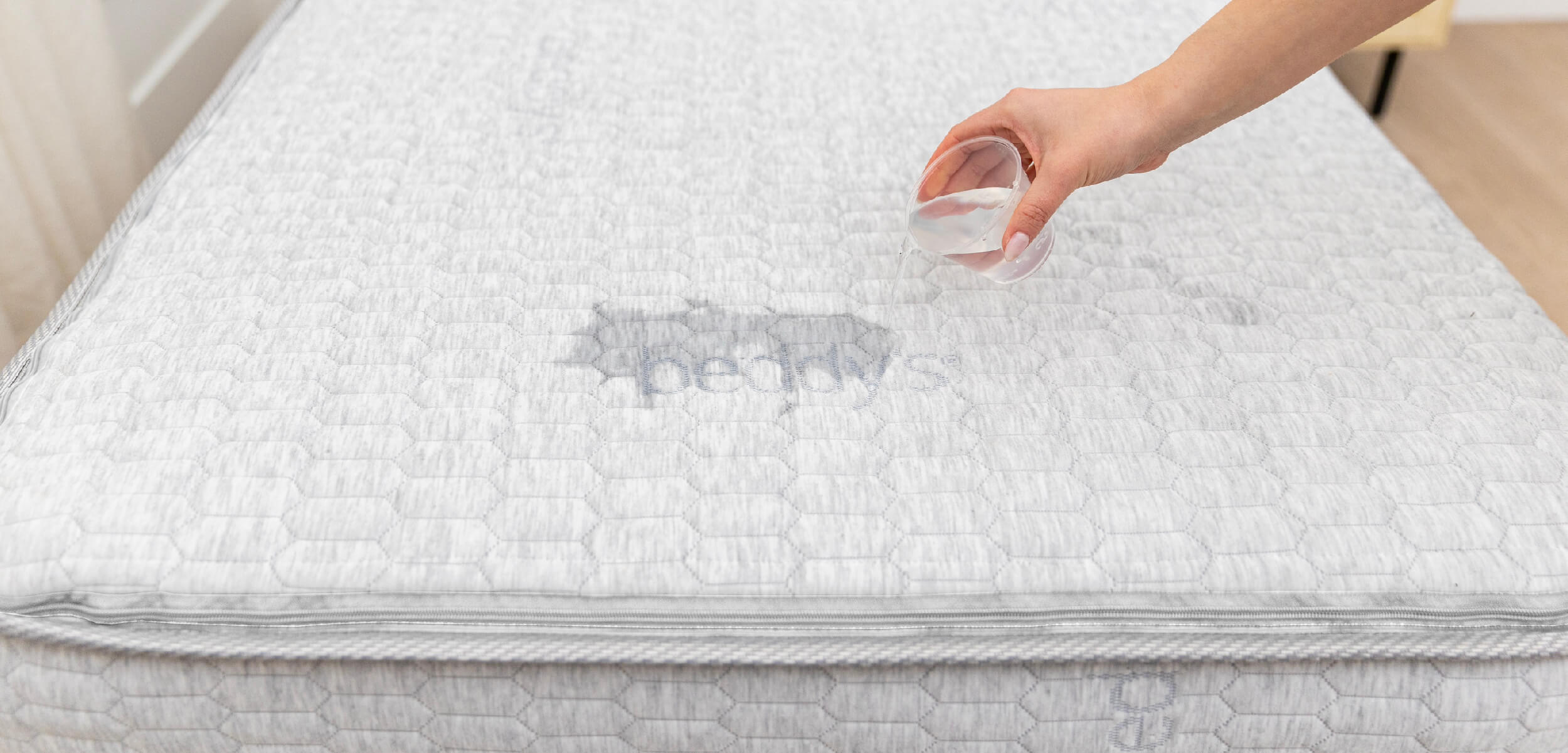 The Beddys ZipClean Mattress with someone pouring a small cup of water over the top to show that it is moisture resistant.