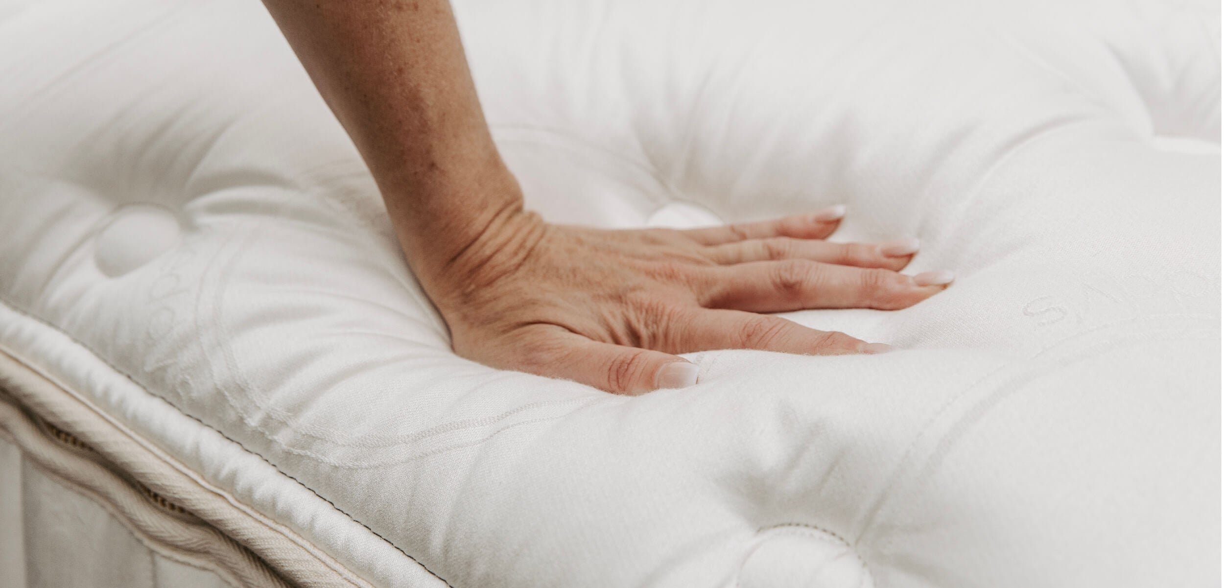 A hand pressing. down on the tufted, luxurious top layer of the Beddys ZipLuxe Mattress to help demonstrate how plush and comfortable it is.