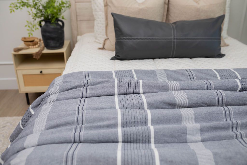 A close up of a bed made with cream embroidered zipper bedding adorned with neutral pillows and a blue striped pattern blanket.