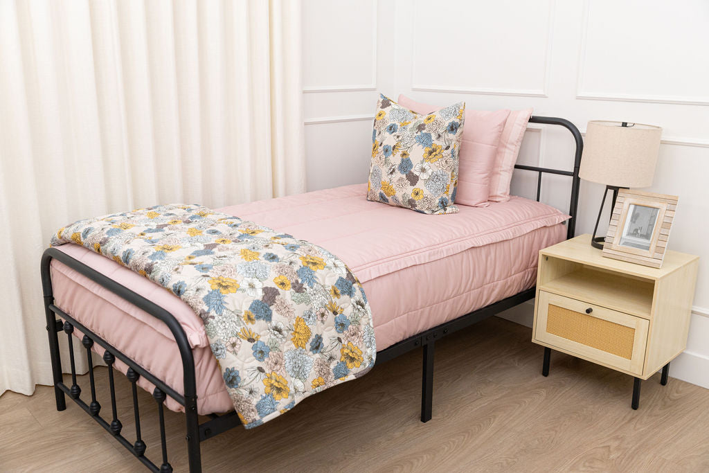 A bed made with pink zipper bedding and an assortment of light pink and floral pillows and blanket.