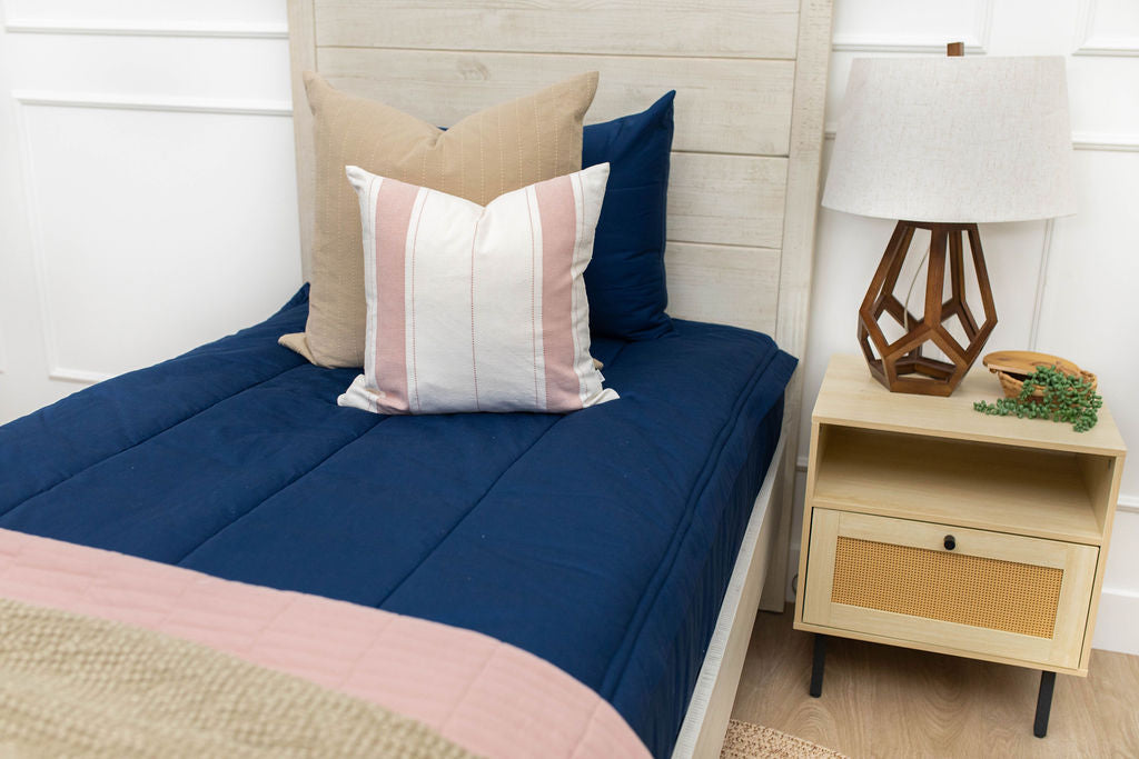 A bed made with navy blue zipper bedding and an assortment of neutral and striped throw pillows and blanket.