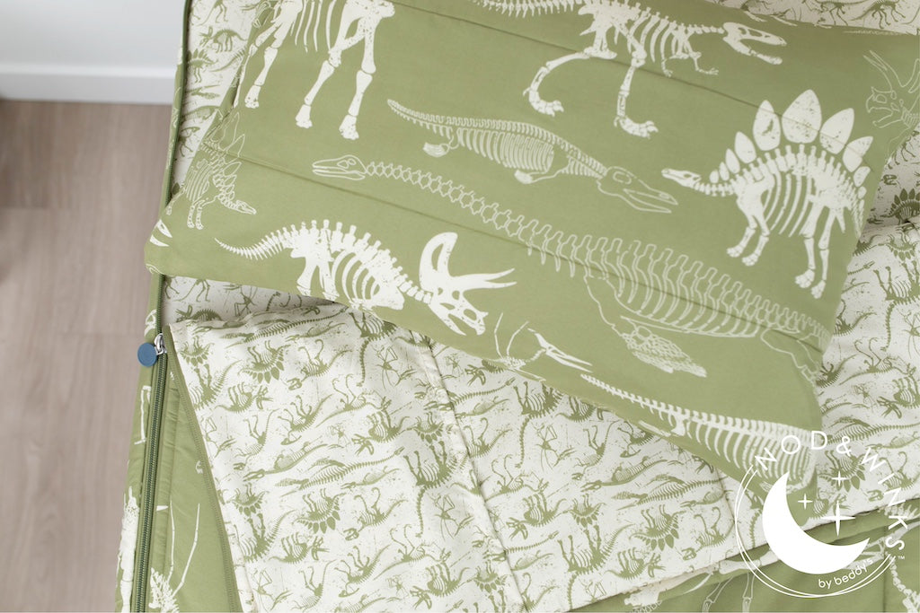 A twin bed made with olive green dinosaur fossils kids zipper bedding, the top unzipped and slightly pulled back and a pillow on the bed.