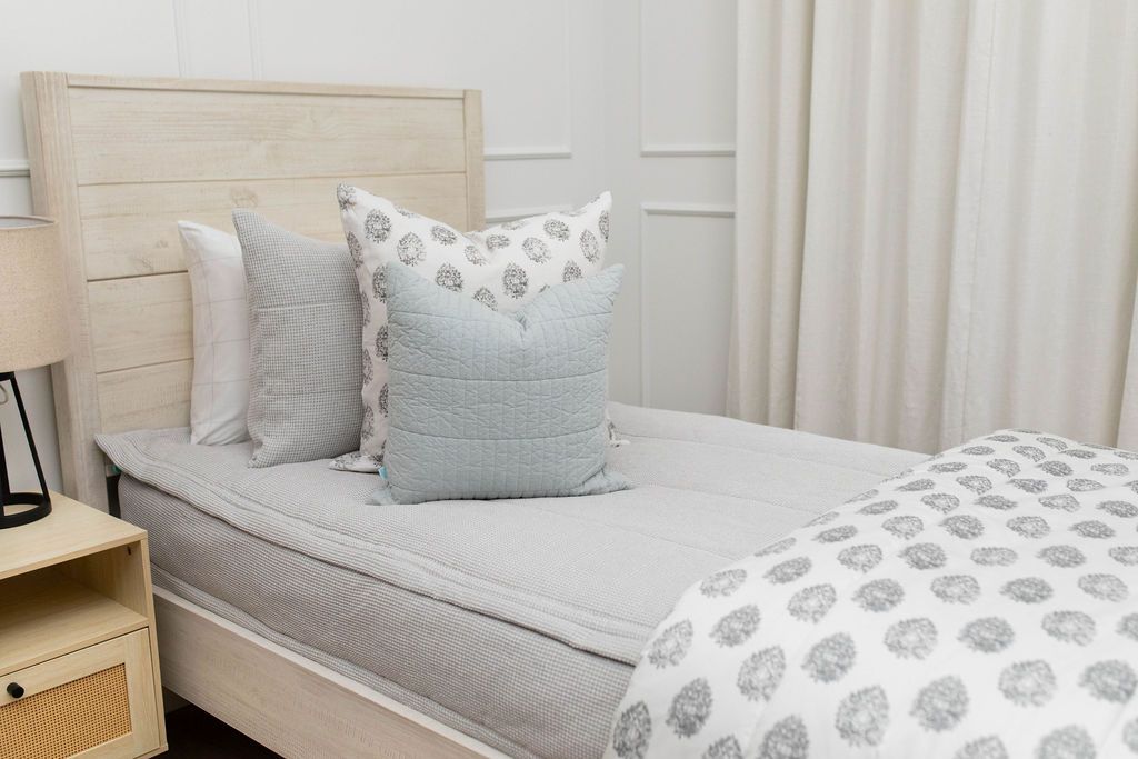 A bed made with light gray waffle texture zipper bedding and an assortment of neutral and striped pillows and blanket.