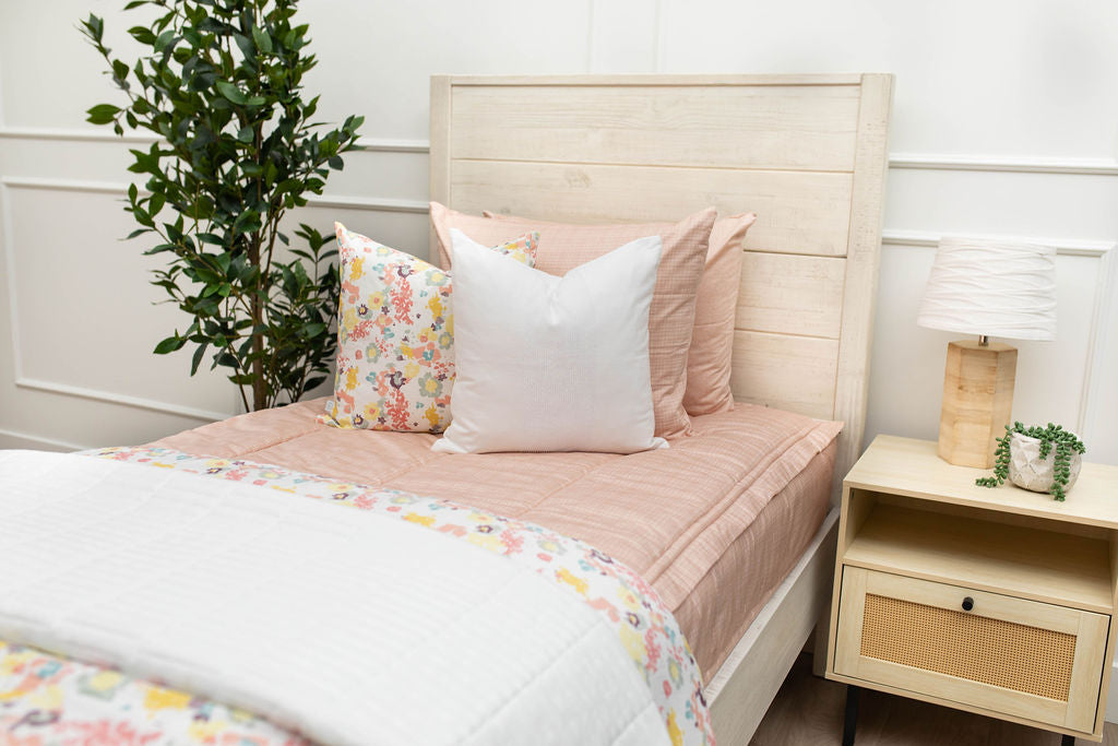 A queen bed made with peach pink zipper bedding adorned with neutral and pink pillows and blankets.