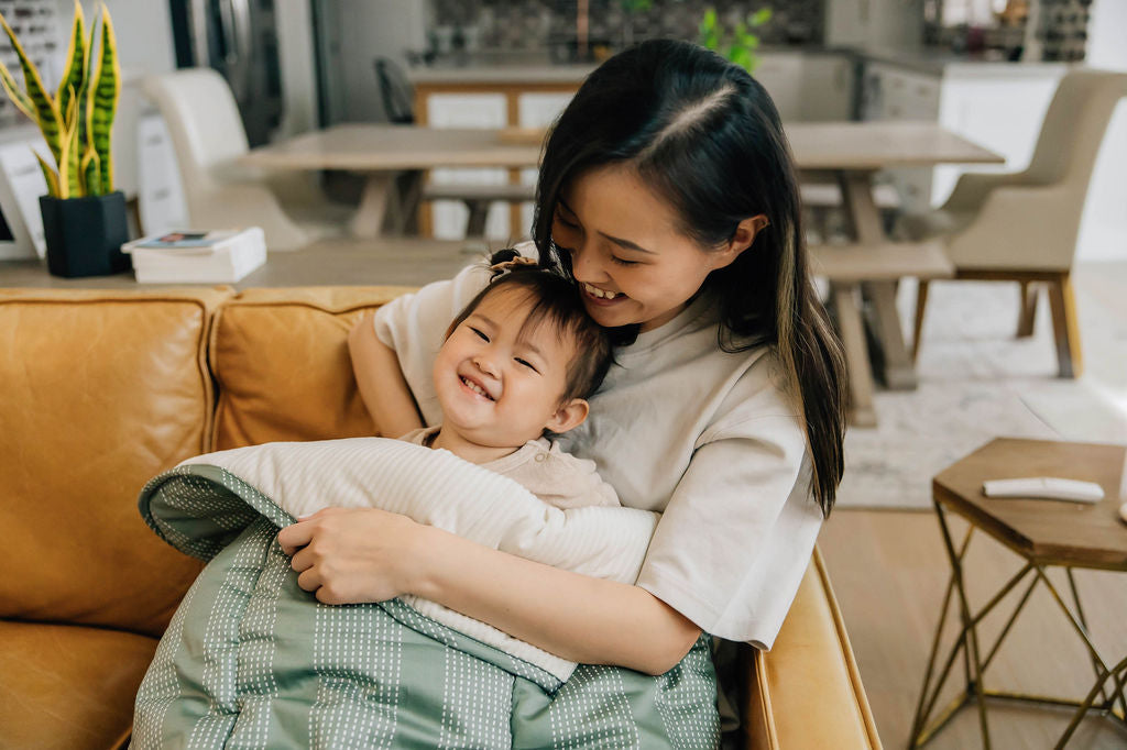 Mother and daughter laughing and cuddling on couch with a green dotted stripe children&