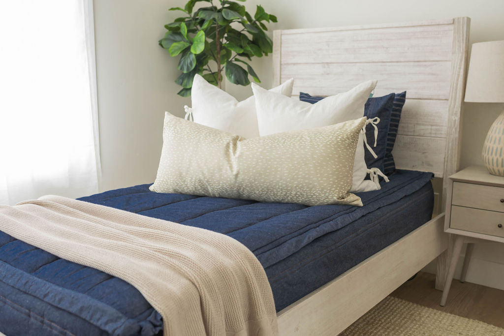 A bed made with dark denim blue zipper bedding and an assortment of neutral throw pillows and a cowboy western printed blanket.