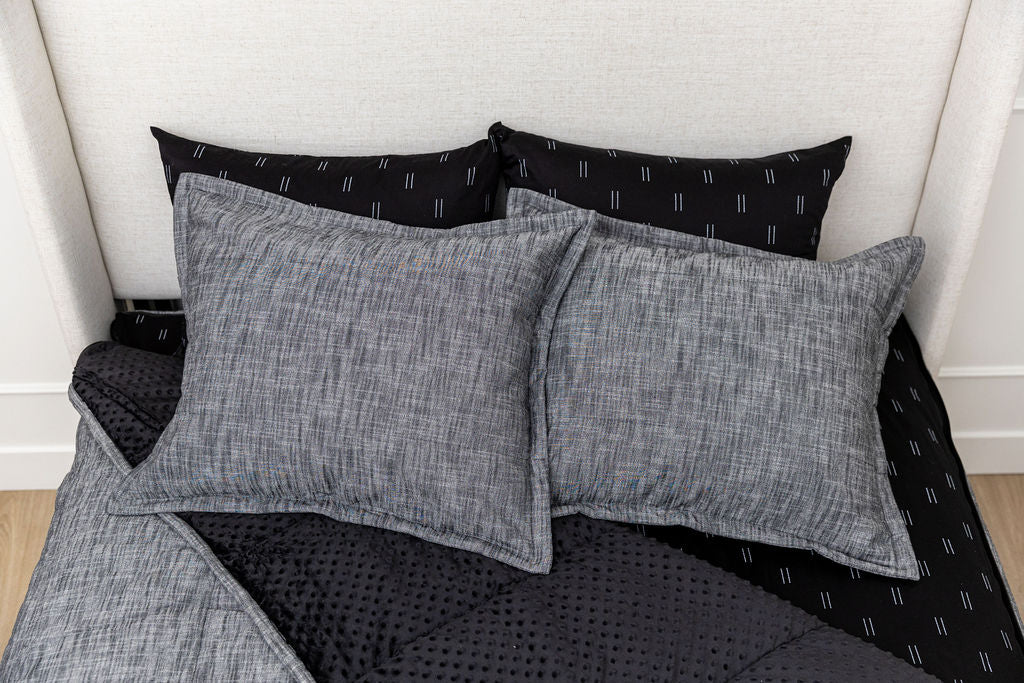 A bed made with dark charcoal gray zipper bedding with the comforter pulled back and pillows on top of the bed.