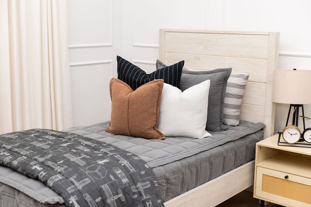 A bed made with gray zipper bedding and an assortment of floral and pink bedding accessories