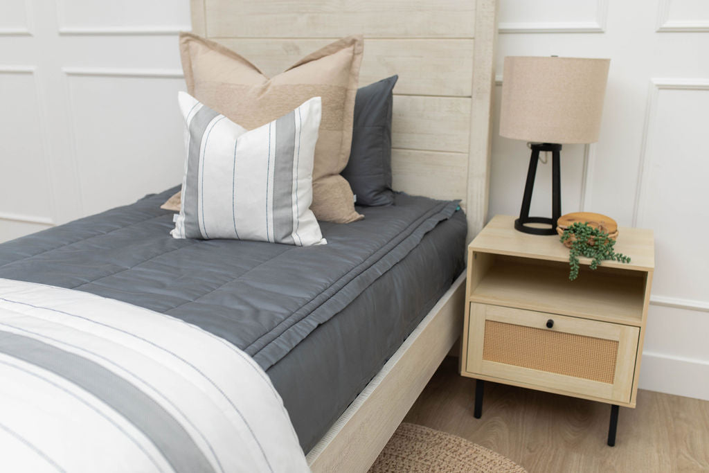 A bed made with gray zipper bedding and an assortment of neutral and striped throw pillows and blanket.