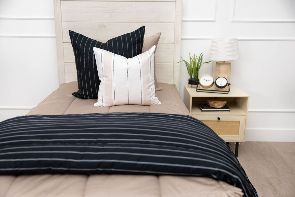 A bed made with tan zipper bedding and an assortment of neutral and black pillows and blanket.
