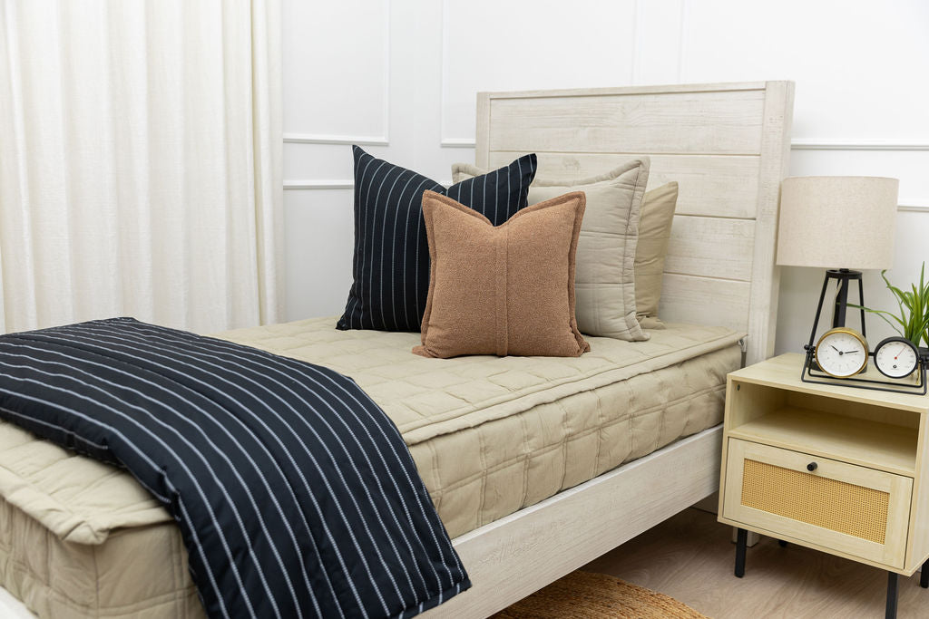 A bed made with khaki zipper bedding and an assortment of cream and leather bedding accessories.