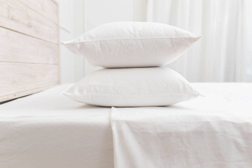 A side shot of a bed made with white sheets, with two pillows stacked on top of the bed.