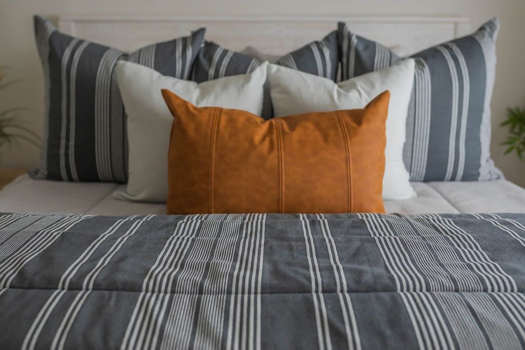 A close up view of a queen bed made with light gray zipper bedding and neutral and dark gray striped pillows and blanket.
