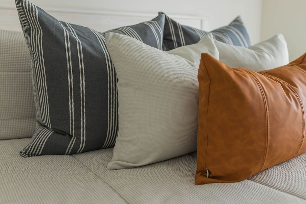 A close up view of a bed made with light gray textured zipper bedding and an assortment of neutral and leather pillows.