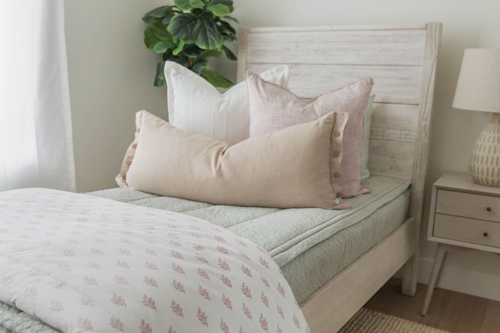 A bed made with soft green zipper bedding and an assortment of pink and multi-color floral pillows and blanket.