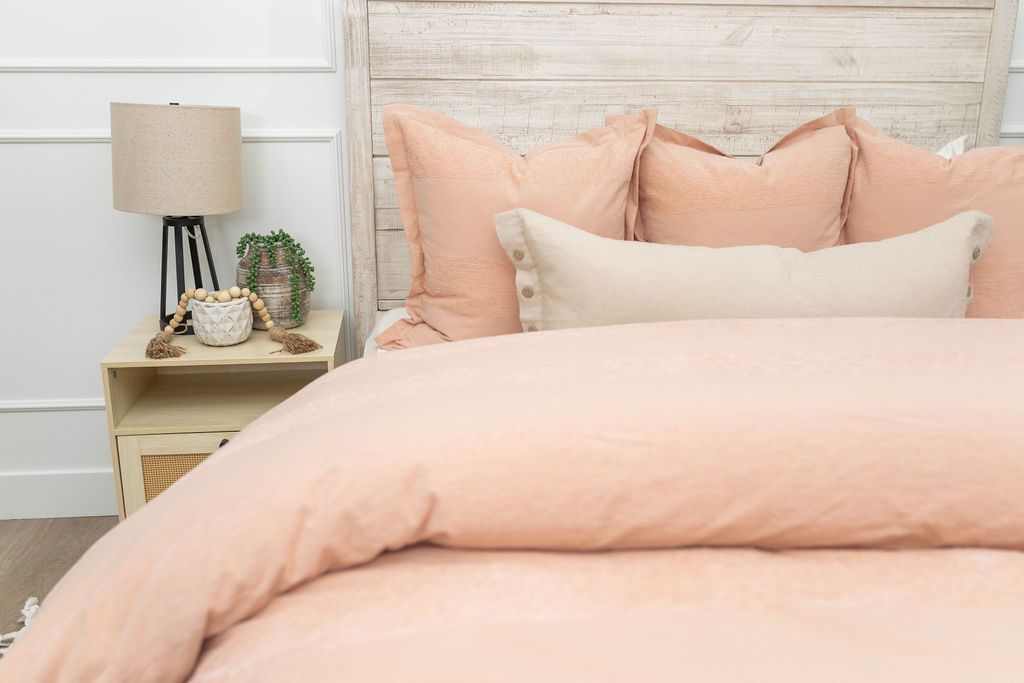 A bed made with a peach zipper duvet folded half way down the bed and adorned with neutral and matching pillows.