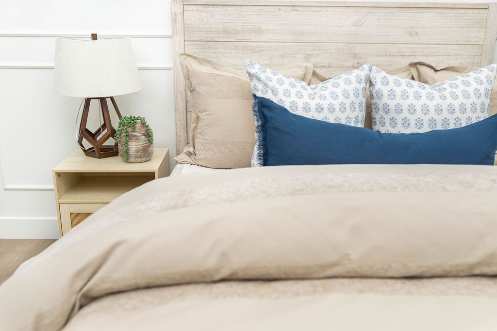 A bed made with a tan zipper duvet folded half way down the bed and adorned with neutral and blue pillows.