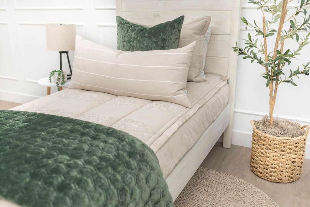 A bed made with tan faded stripes zipper bedding and an assortment of neutral and blue velvet throw pillows and blankets.