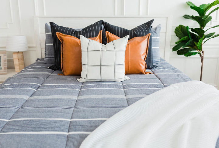 A bed in a brightly lit room made with striped zipper bedding.